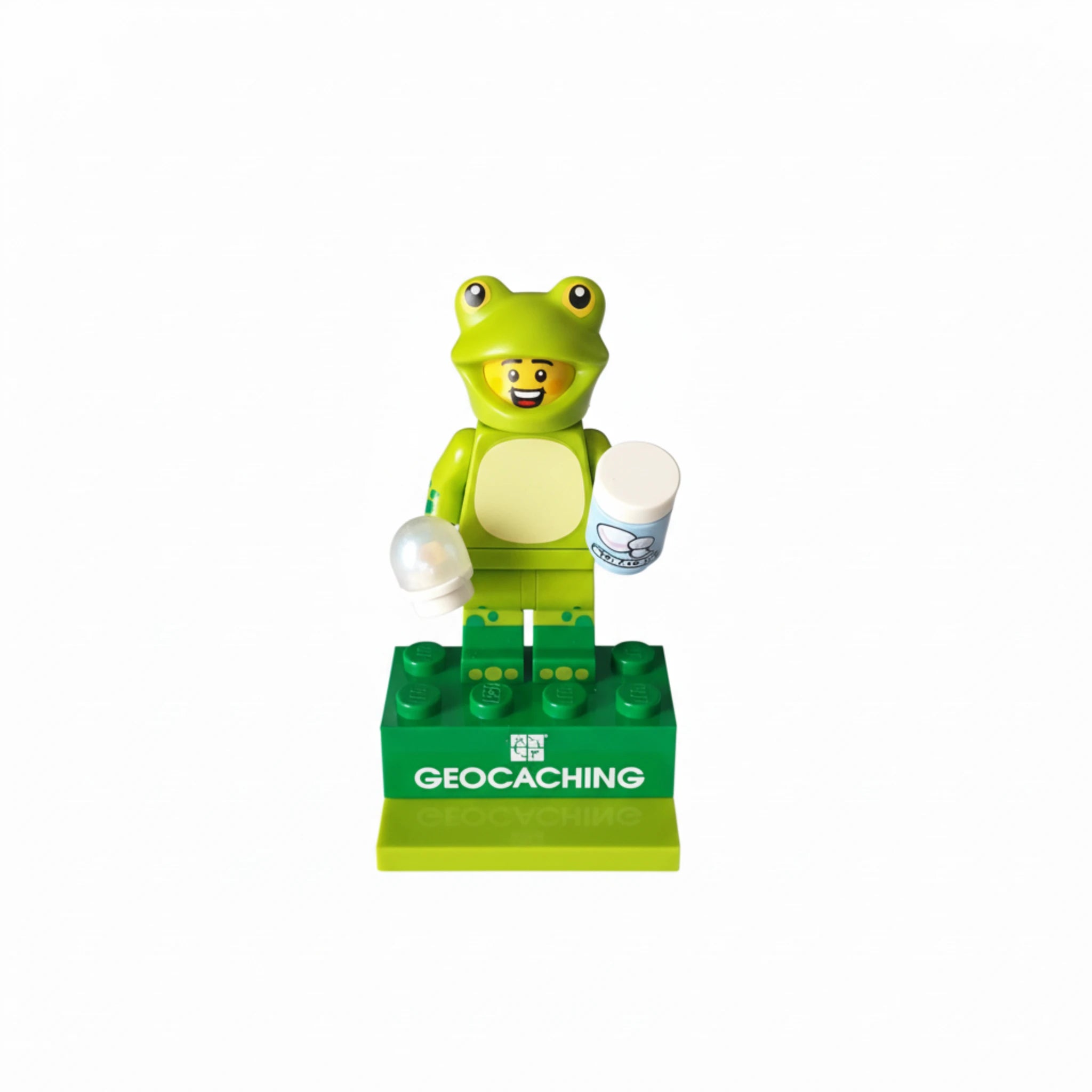 Lego-style frog suit geocaching figure holding cache containers on green geocaching display base