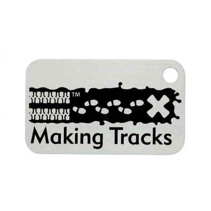 Black Making Tracks metal trackable tag with tyre tracks, footprints and X design on a white background